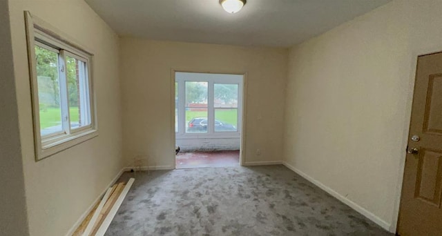 carpeted spare room featuring a healthy amount of sunlight and baseboards