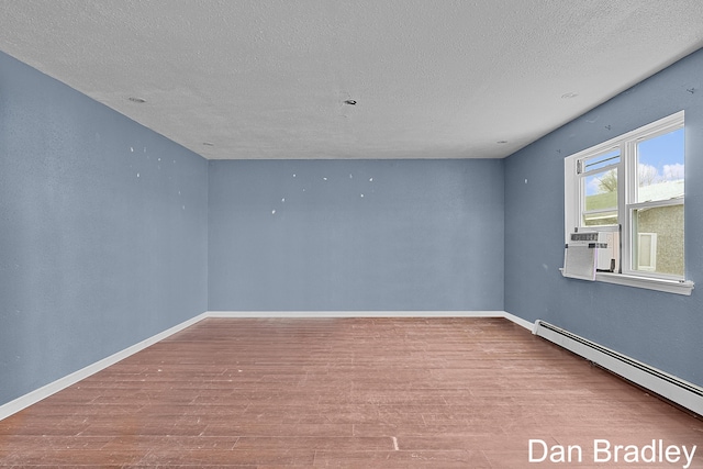 spare room featuring a baseboard heating unit, baseboards, wood finished floors, and a textured ceiling