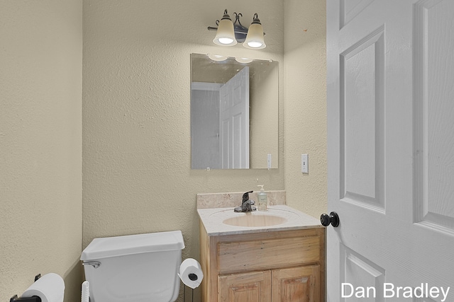 half bathroom with a textured wall, toilet, and vanity