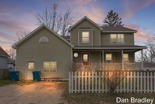 back of property at dusk featuring covered porch and fence