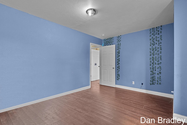 spare room with wood finished floors, a textured ceiling, and baseboards