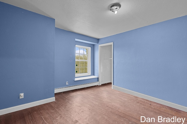 unfurnished room featuring a baseboard heating unit, wood finished floors, a textured ceiling, and baseboards