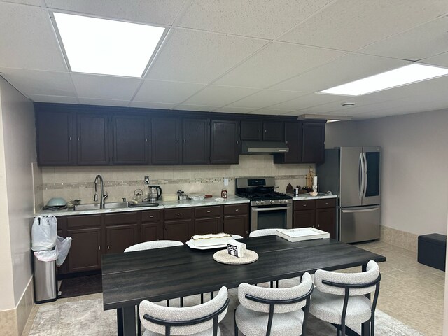 kitchen featuring appliances with stainless steel finishes, under cabinet range hood, a sink, light countertops, and backsplash