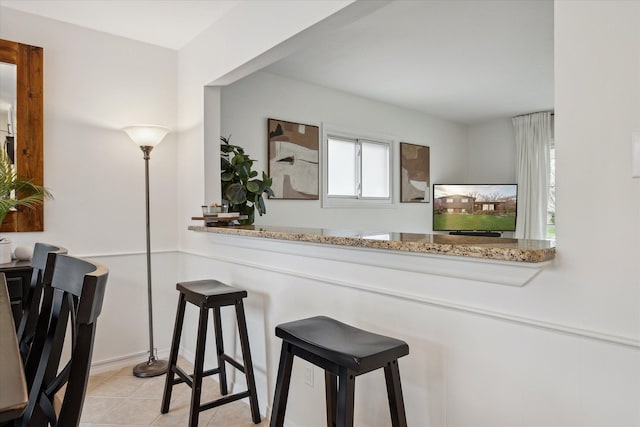kitchen with light tile patterned flooring, stone counters, and a breakfast bar area
