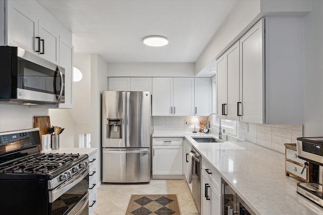 kitchen with stainless steel appliances, a sink, white cabinetry, decorative backsplash, and light stone countertops