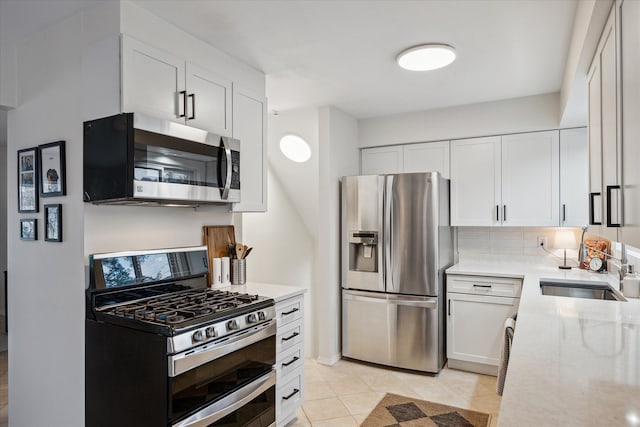 kitchen featuring white cabinets, stainless steel appliances, a sink, light tile patterned flooring, and light stone countertops