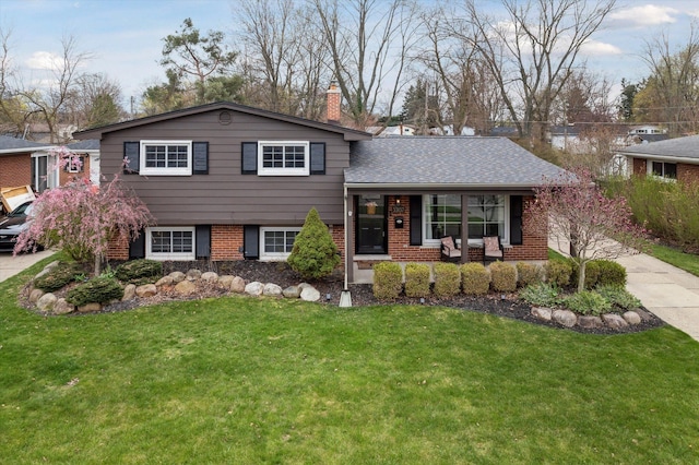 tri-level home with a chimney, covered porch, a front yard, and brick siding