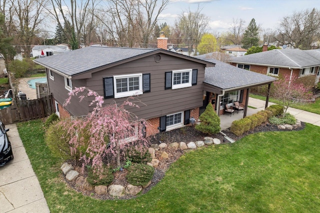 view of front of property featuring a patio area, a chimney, a front lawn, fence, and brick siding