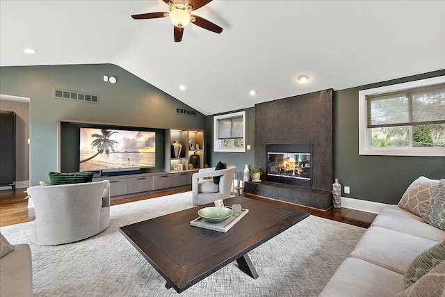 living room with a wealth of natural light, visible vents, lofted ceiling, wood finished floors, and a fireplace