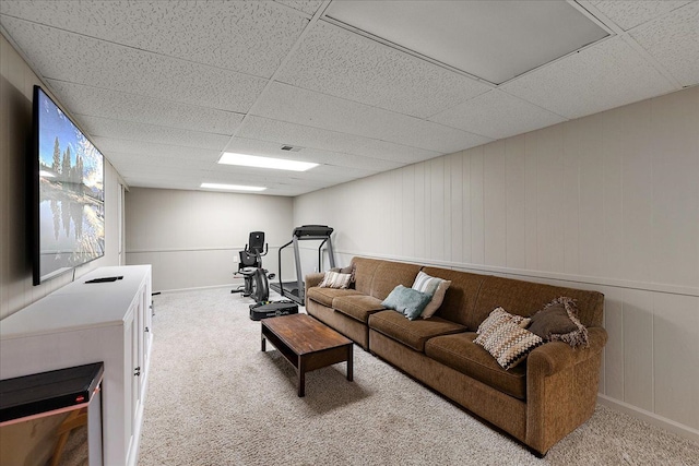 carpeted living room featuring a decorative wall, a drop ceiling, and baseboards