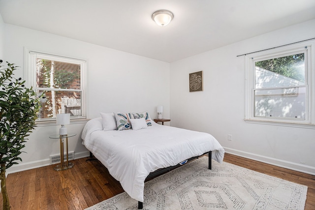 bedroom with baseboards, wood finished floors, multiple windows, and visible vents