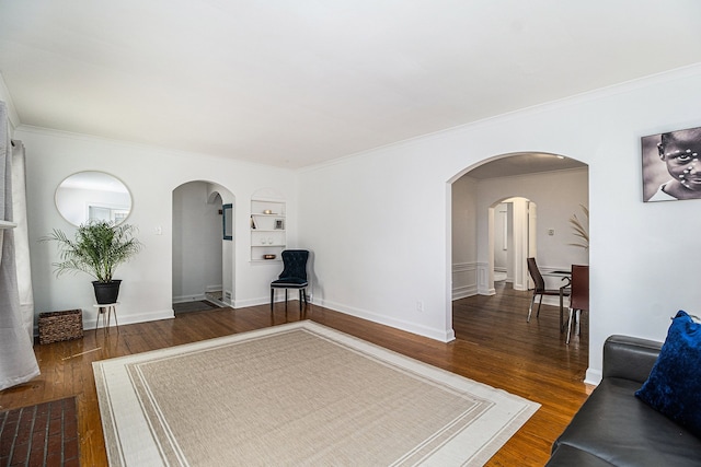living area with arched walkways, baseboards, built in shelves, wood finished floors, and crown molding