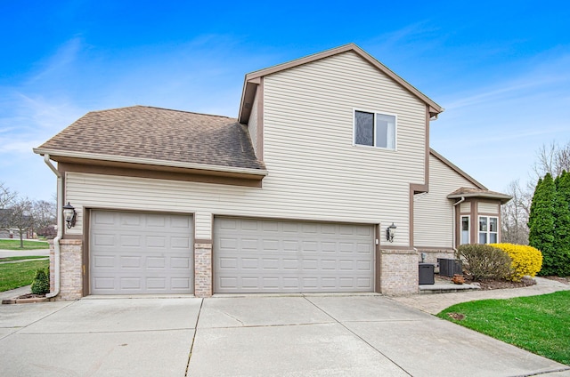 exterior space featuring driveway, a shingled roof, cooling unit, a garage, and brick siding