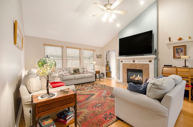 living room with high vaulted ceiling, a ceiling fan, a tile fireplace, and light wood finished floors