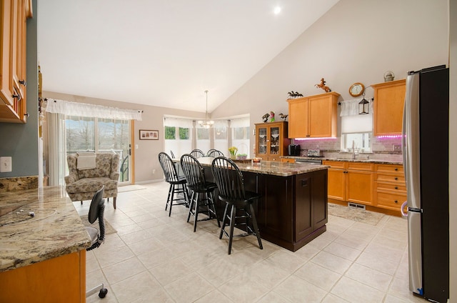 kitchen with a kitchen breakfast bar, stainless steel appliances, visible vents, a sink, and high vaulted ceiling