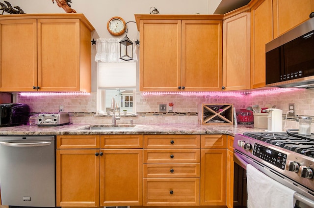 kitchen with appliances with stainless steel finishes, tasteful backsplash, a sink, and light stone countertops