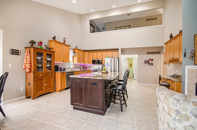 kitchen with a high ceiling, light tile patterned floors, stainless steel appliances, and visible vents