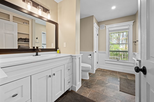 2457 Rocky Top Ln, Commerce Twp, MI 48382 - bathroom featuring stone tile flooring, toilet, wainscoting, vanity, and recessed lighting