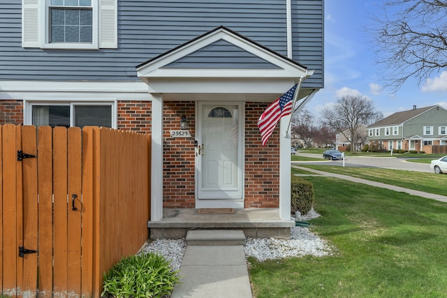 doorway to property featuring fence, brick siding, and a yard