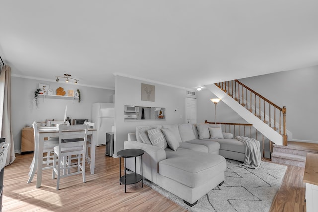 living room with light wood-style flooring, visible vents, stairway, and crown molding