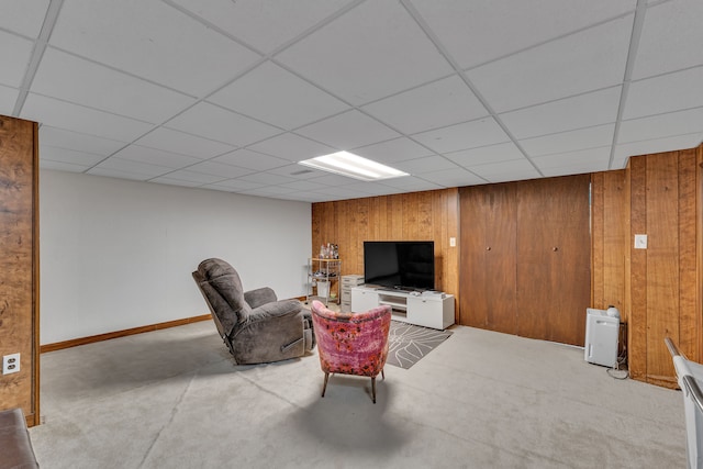carpeted living room featuring wooden walls and a drop ceiling