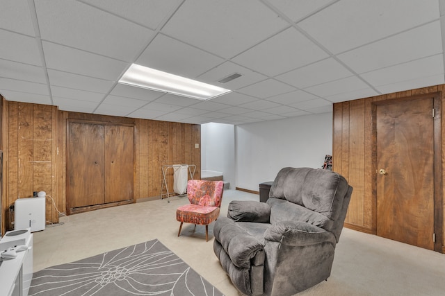living area featuring wooden walls, carpet flooring, a drop ceiling, and visible vents