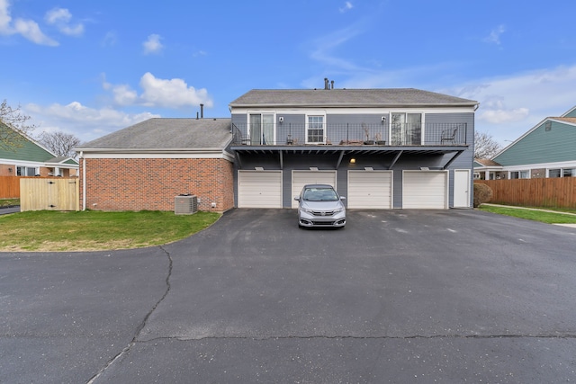 view of front of home featuring aphalt driveway, fence, a balcony, an attached garage, and brick siding