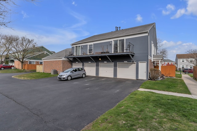 traditional-style house with central air condition unit, driveway, fence, an attached garage, and a balcony