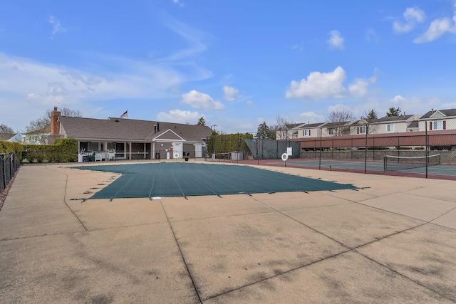 view of swimming pool with fence, a residential view, and a tennis court