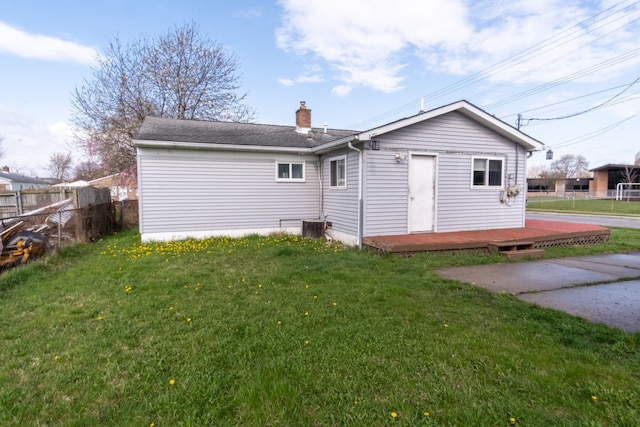 rear view of house with a wooden deck, a yard, a chimney, and fence