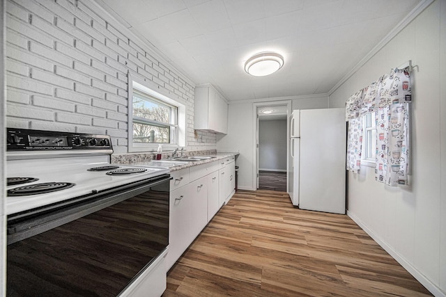 kitchen featuring light countertops, electric range, white cabinets, ornamental molding, and freestanding refrigerator
