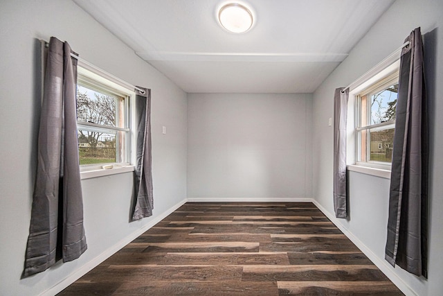empty room featuring a wealth of natural light, dark wood-type flooring, and baseboards