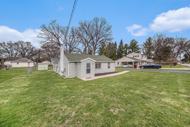 exterior space featuring driveway, a shingled roof, a front lawn, and fence