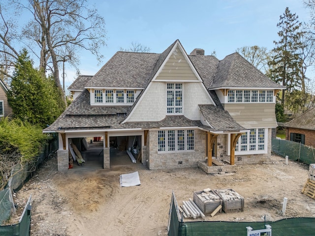 view of front of house with a chimney, a fenced backyard, stone siding, dirt driveway, and roof with shingles