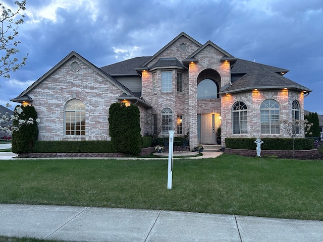 french country style house with a front yard, roof with shingles, and brick siding