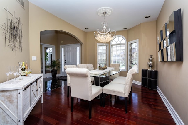 dining area with visible vents, arched walkways, dark wood-type flooring, a wealth of natural light, and a notable chandelier