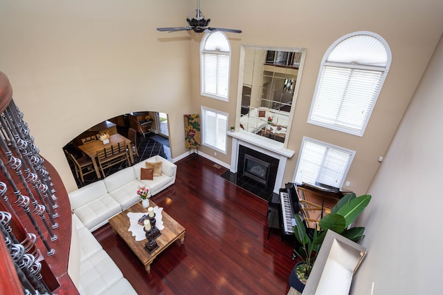 living room featuring a tiled fireplace, ceiling fan, baseboards, a towering ceiling, and wood finished floors