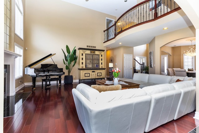 living area with arched walkways, wood finished floors, visible vents, a notable chandelier, and a high ceiling