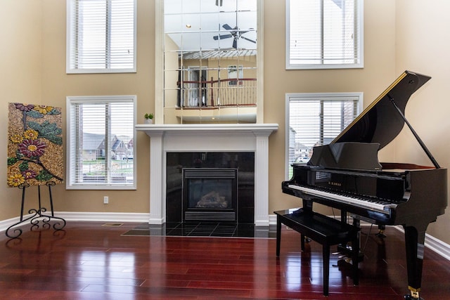 sitting room featuring baseboards, a fireplace, wood finished floors, a ceiling fan, and a high ceiling