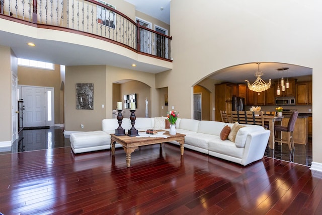 living area with wood finished floors, a chandelier, arched walkways, baseboards, and a high ceiling