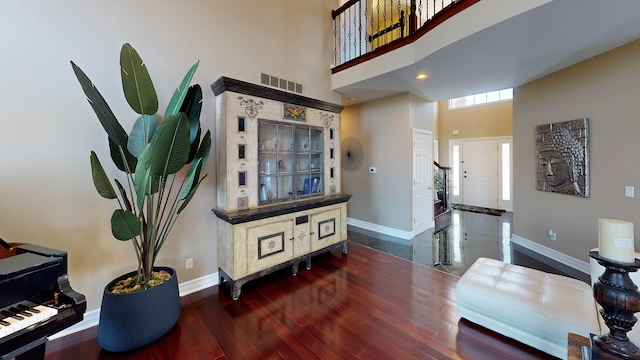 interior space with a towering ceiling, visible vents, dark wood-type flooring, and baseboards