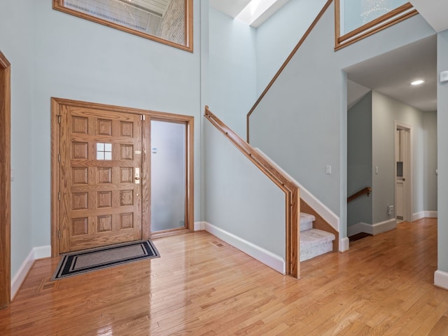foyer entrance with baseboards, wood finished floors, a towering ceiling, and stairway