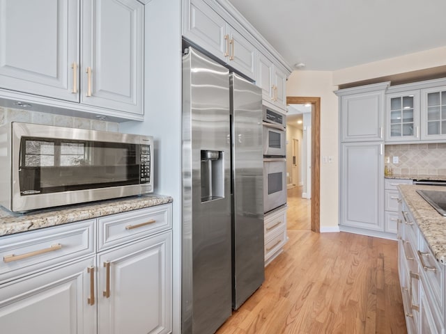 kitchen featuring glass insert cabinets, light wood-type flooring, white cabinetry, backsplash, and appliances with stainless steel finishes