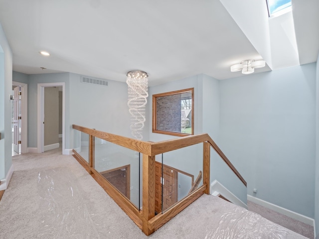 hallway featuring carpet floors, an upstairs landing, visible vents, and baseboards