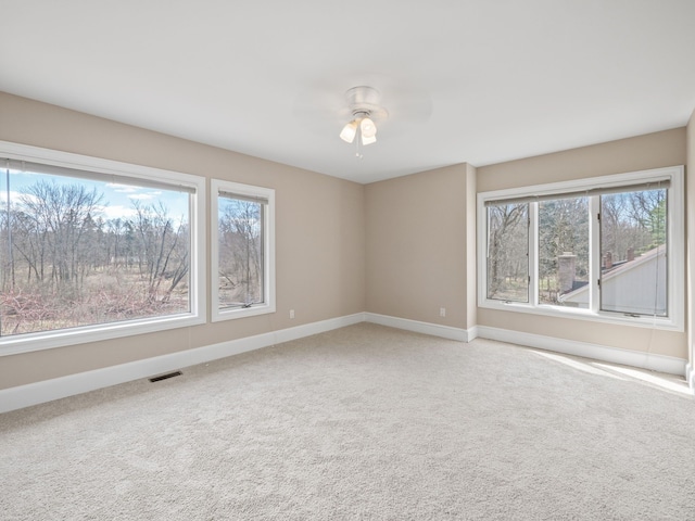 empty room featuring visible vents, light carpet, baseboards, and ceiling fan