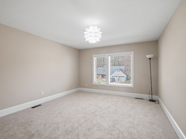 spare room with visible vents, baseboards, a chandelier, and light colored carpet