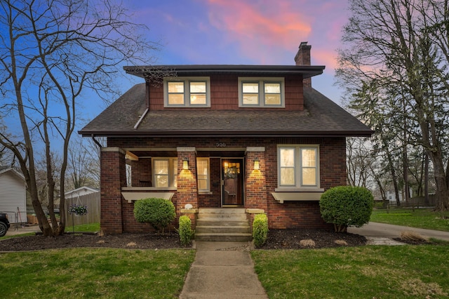 view of front of home with covered porch, a front lawn, brick siding, and a chimney