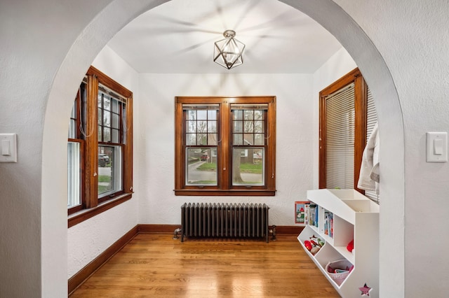 hall with arched walkways, radiator, baseboards, and wood finished floors