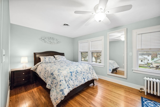 bedroom featuring wood finished floors, ceiling fan, radiator, baseboards, and visible vents