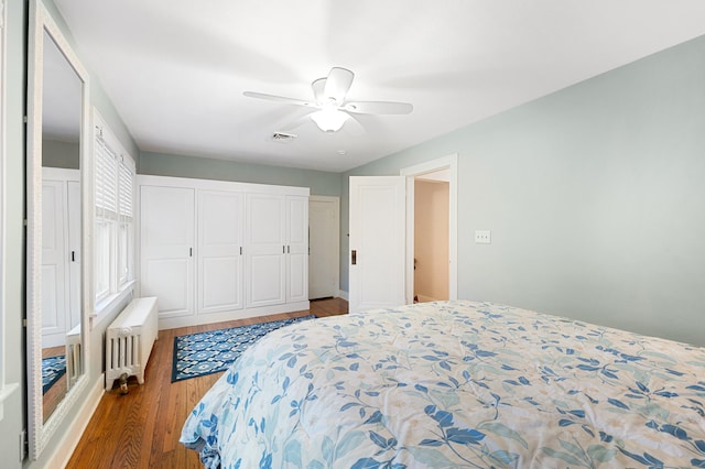 bedroom featuring radiator, wood finished floors, visible vents, a ceiling fan, and a closet